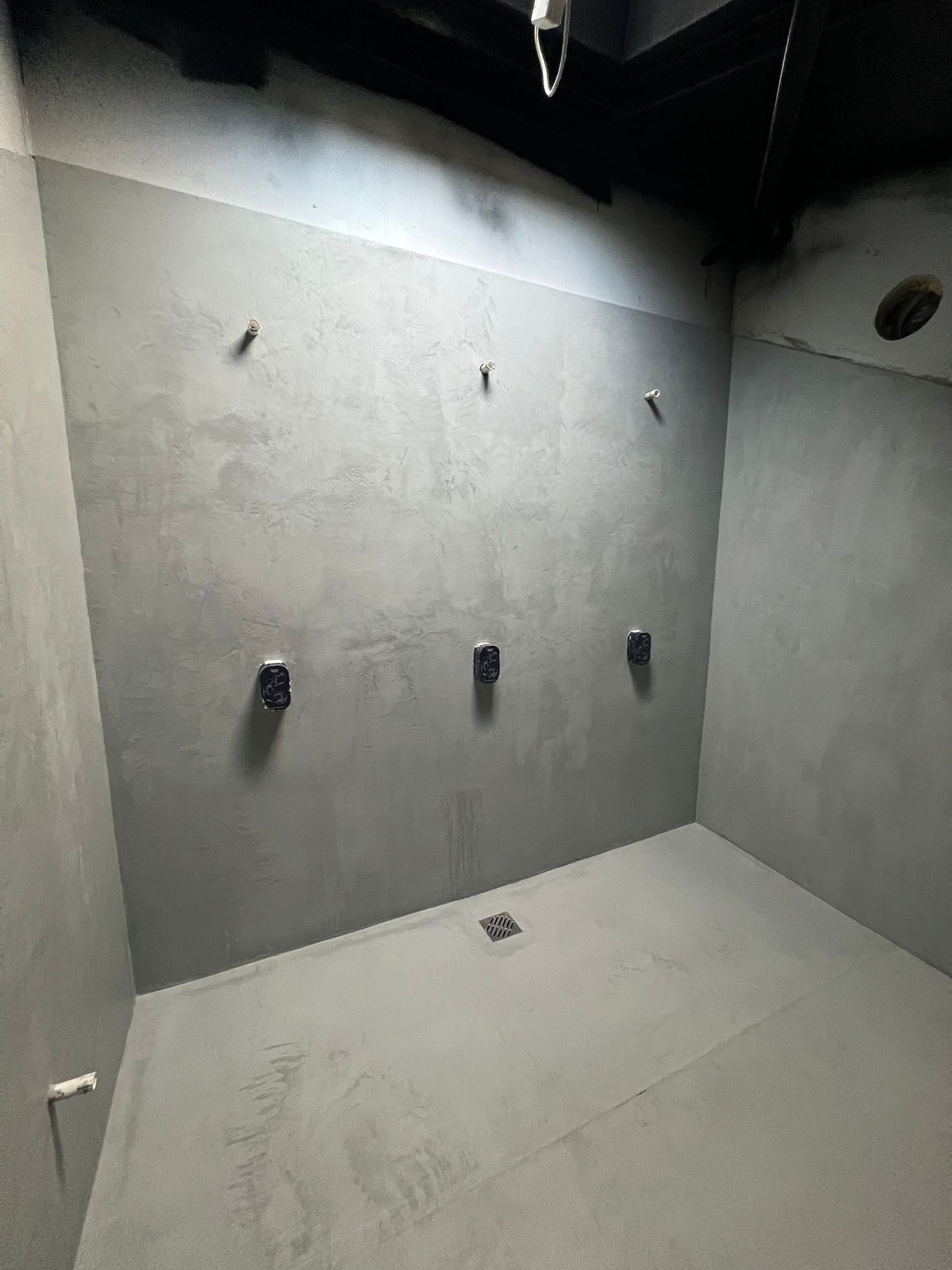 Graue fugenlose Wand- und Bodenoberflächen in einem Duschbereich während des Ausbaus